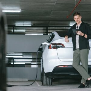 Person leaning on a white car while waiting to charge their electric vehicle at a charging station in Vancouver