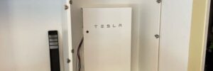 A close-up shot shows a white, rectangular Tesla Powerwall home battery unit