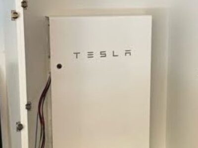 A close-up shot shows a white, rectangular Tesla Powerwall home battery unit