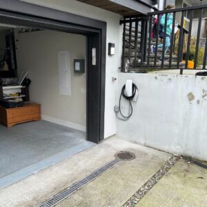 A garage with an open door, a Tesla charging connector on the wall, and a person walking on stairs in the background