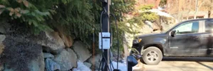 SWTCH Canadian-made EV charging station mounted on a post in a residential North Vancouver driveway, surrounded by rocks and conifer trees with a black truck parked nearby