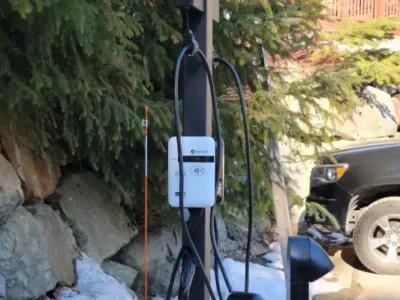 SWTCH Canadian-made EV charging station mounted on a post in a residential North Vancouver driveway, surrounded by rocks and conifer trees with a black truck parked nearby