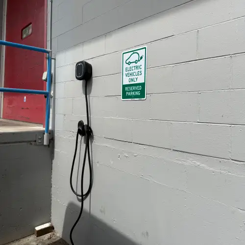 Close-up of a wall-mounted commercial EV charging station and a 'Reserved Parking for Electric Vehicles Only' sign, showcasing expert commercial EV charging installation Vancouver by TCA Electric.