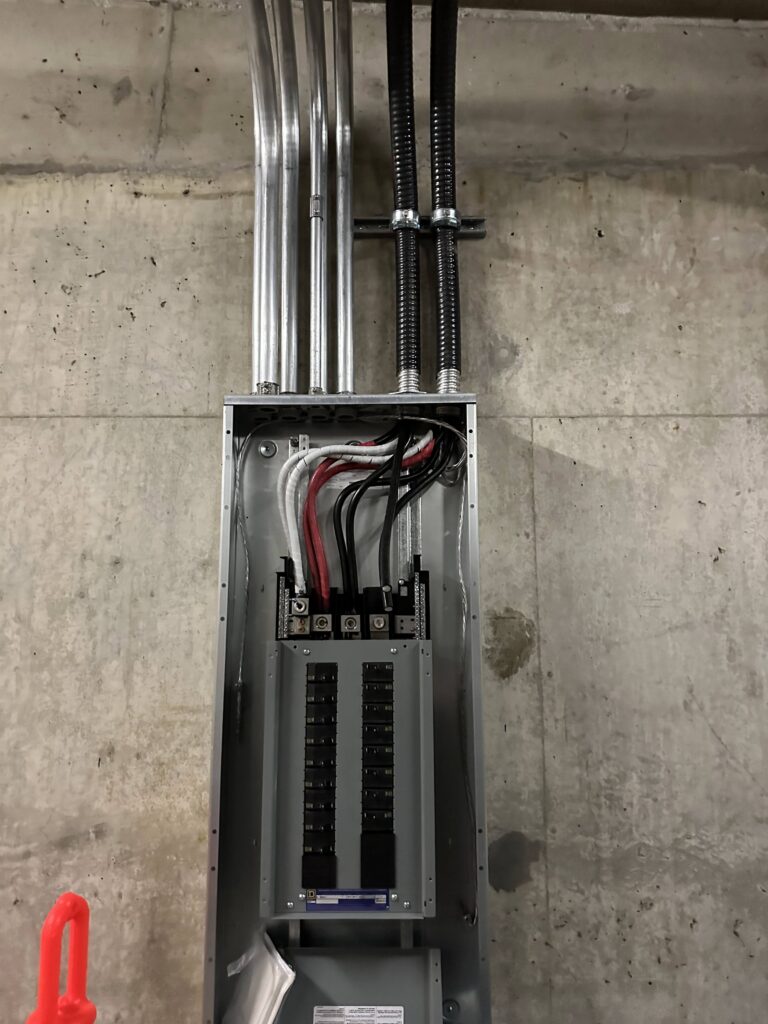 An electrical panel inspection with exposed wiring and conduit against a concrete wall, showing a residential electrical inspection in Vancouver by TCA Electric.