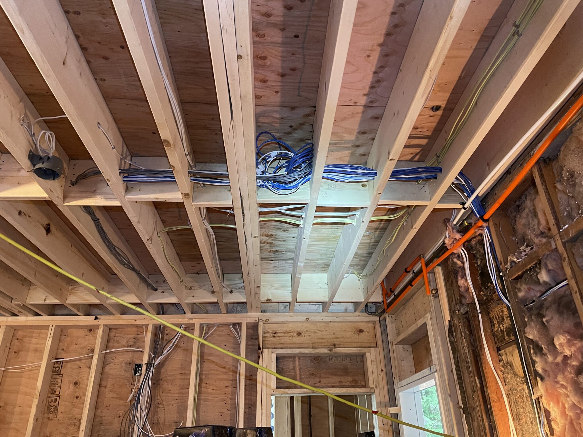 Organized blue and white communication cables and power wiring routed through exposed wooden ceiling joists during a basement suite electrical installation in North Vancouver by TCA Electric.